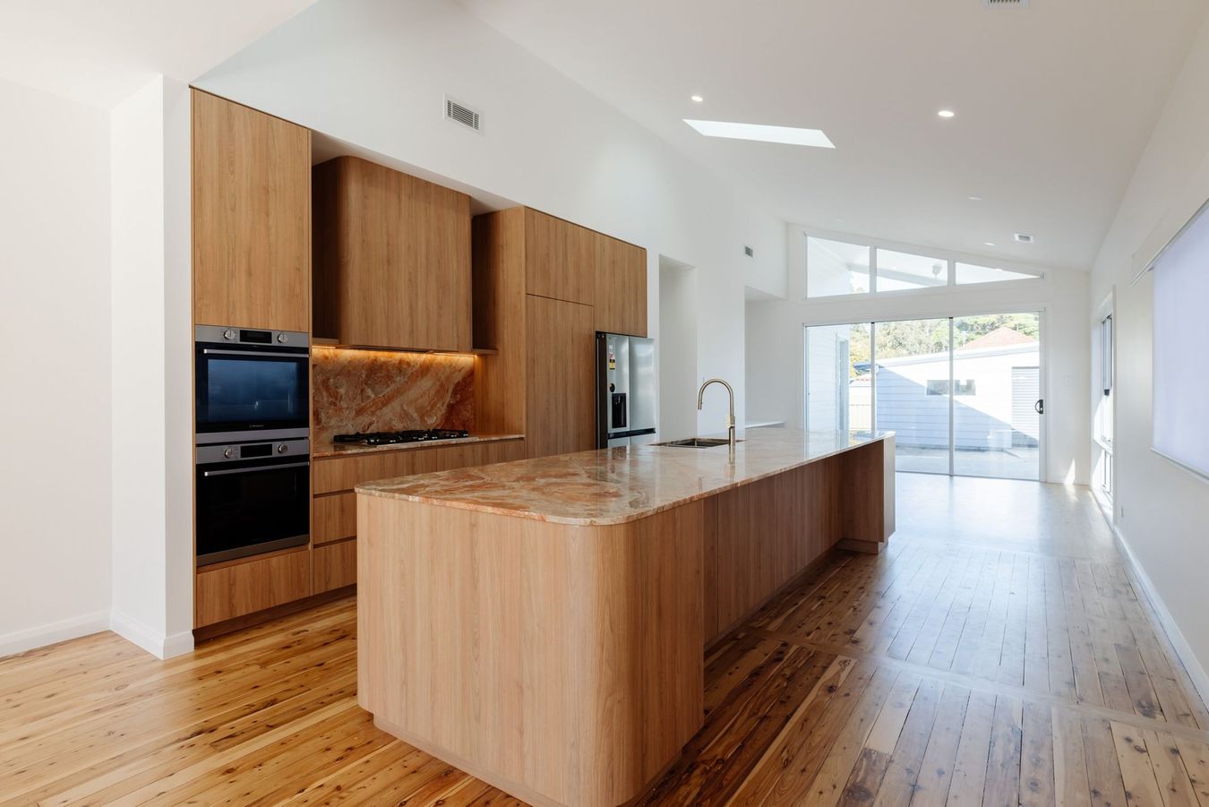 A modern kitchen features a dark blue island with a white countertop, three pendant lights, and a stainless steel fridge.