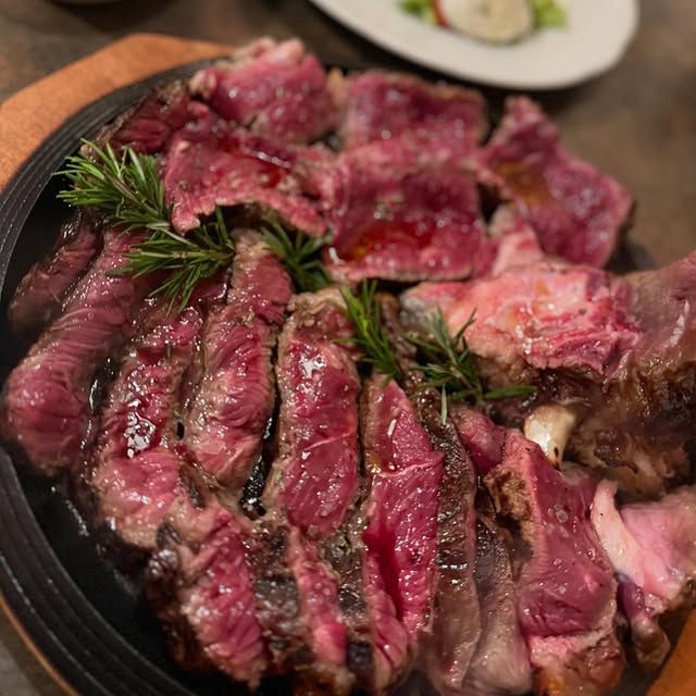 Una bistecca al sangue tagliata a fette e guarnita con rosmarino, adagiata su un piatto scuro, con un contorno sfocato sullo sfondo.