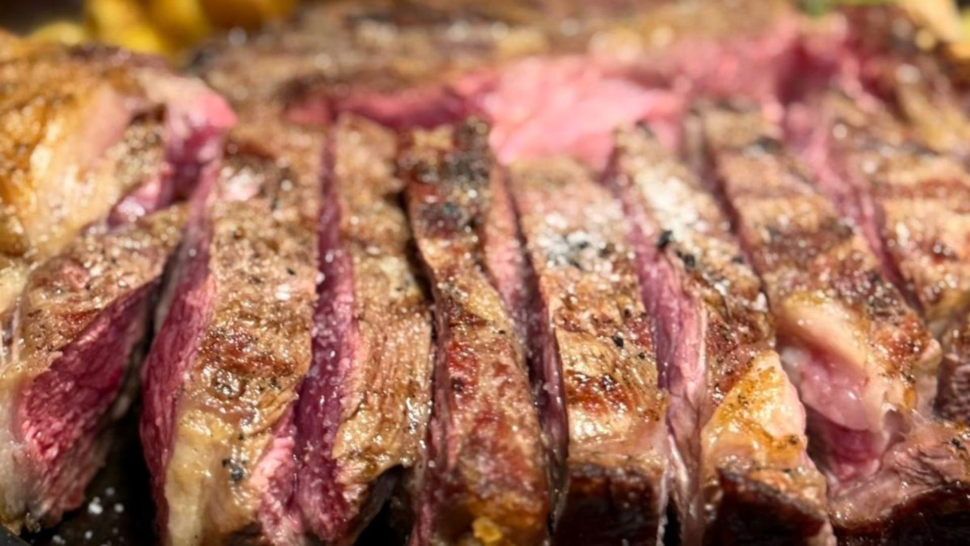 Fette di bistecca grigliata al sangue, con crosticina dorata e interno rosato, servite su un piatto.