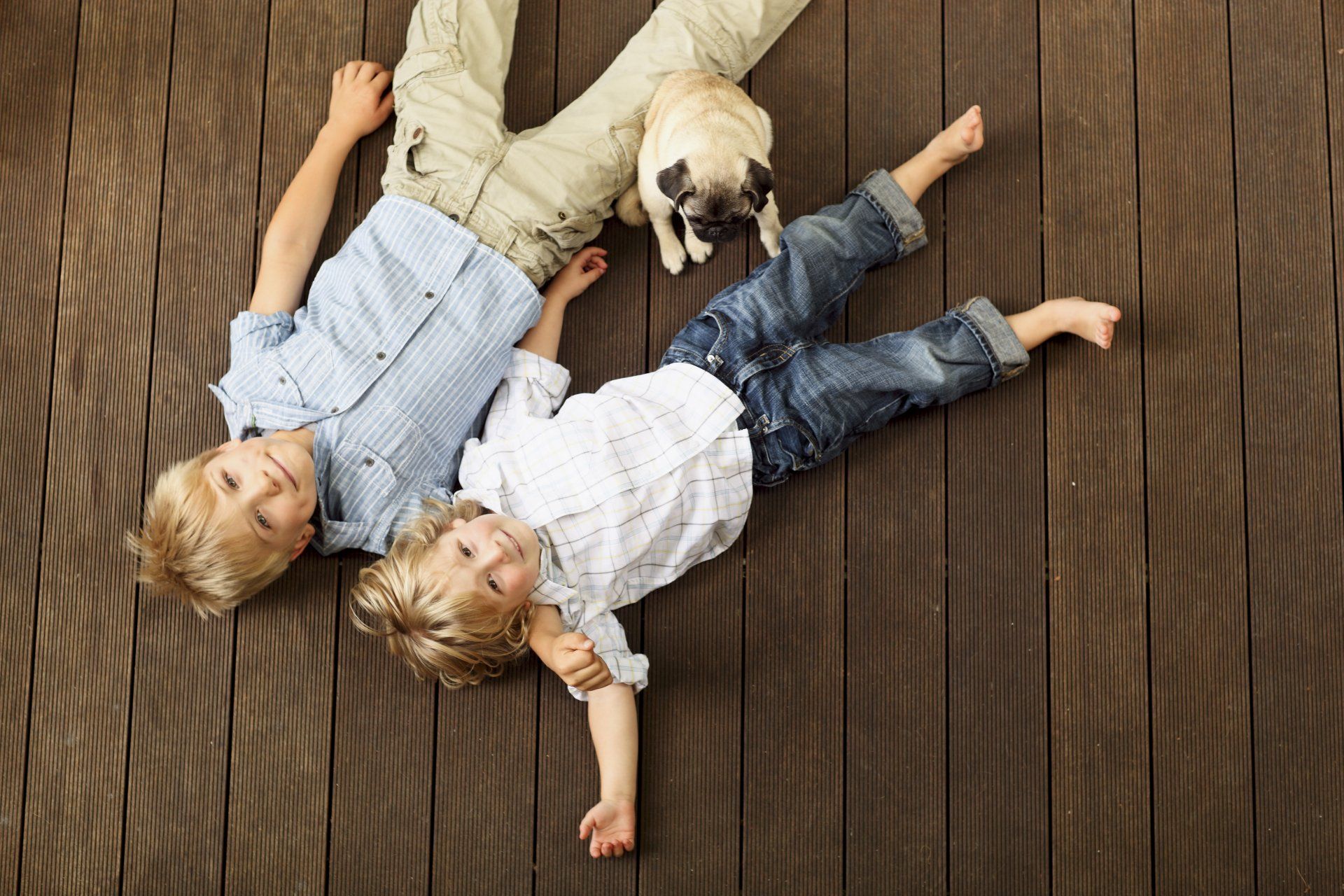 Two children lying down flat on backyard deck with dog