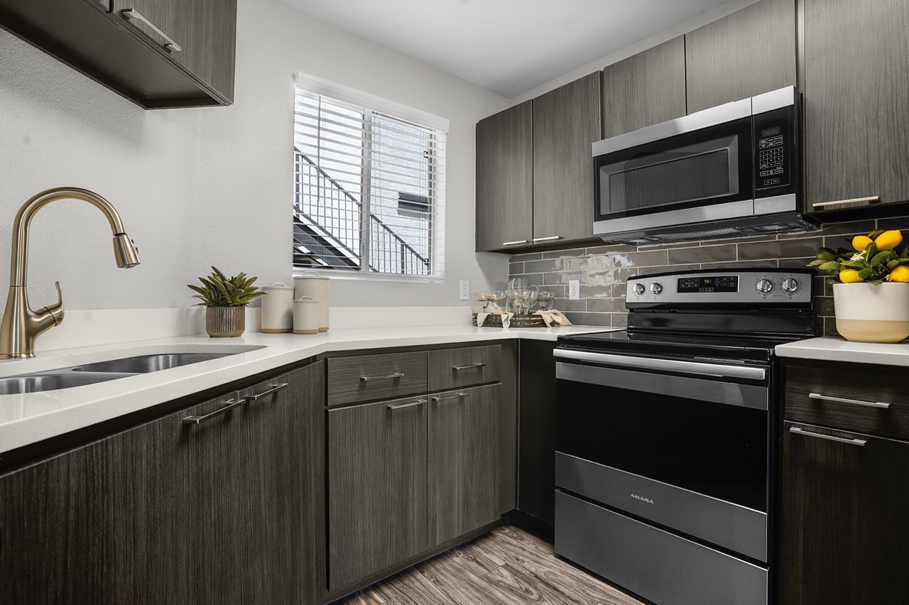 U-shaped kitchen with dark wood cabinets, stainless steel stove and microwave, and a window above the sink at Broadstone Heights in Albuquerque, NM.