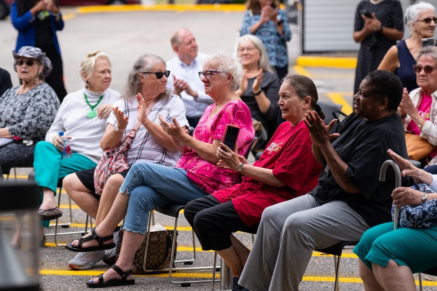Primeplus Members seated outdoors, clapping. Some wear sunglasses and casual clothes. Others stand in the background.