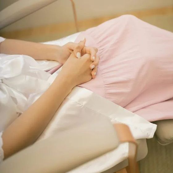 Hands clasped together on a white bed beside a pink pillow.