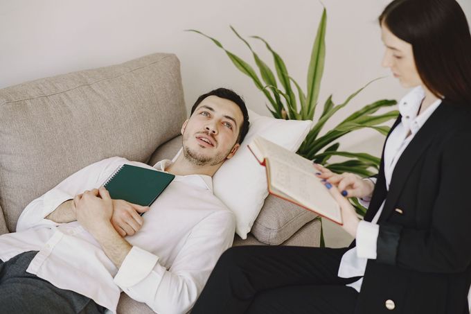 Man reclining on a sofa while a woman in business attire takes notes beside him.