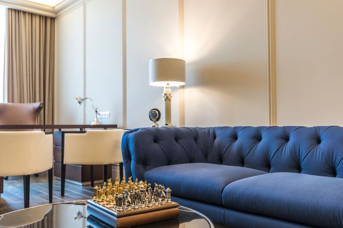 Elegant living room with blue tufted sofa, lamp, chess set, and beige curtains.