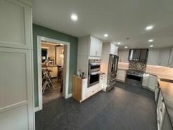 Kitchen with white cabinets, stainless steel appliances, and dark gray flooring. Doorway to a dining area.
