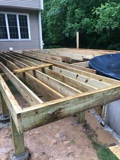 Wooden deck under construction with exposed joists, next to a house and a black object.