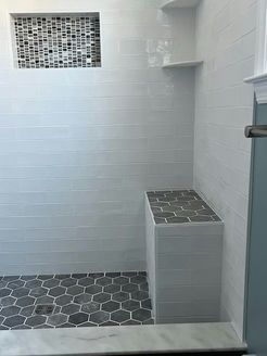 Shower with white tiled walls, gray honeycomb floor, and a built-in bench.