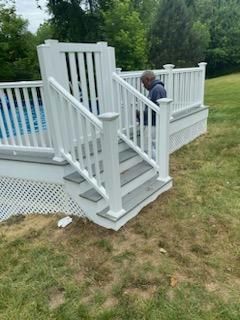 White deck with stairs leading to a pool, person on deck. Gray steps and trim. Grassy yard.