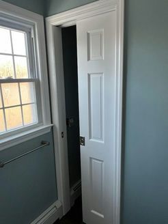 White pocket door in a bathroom with teal walls, open to reveal a dark space.  Window to the left.