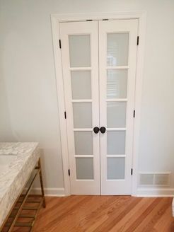 White French doors with frosted glass panels, black hardware, and wood flooring.