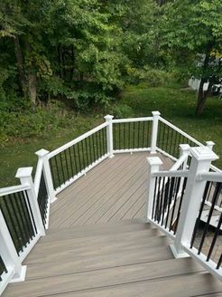 Wooden deck with white railing and black spindles, overlooking a green yard and trees.