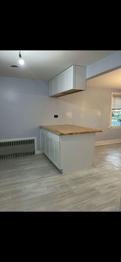 Kitchen with white cabinets, island with wood countertop, light blue walls, and light-colored floor.