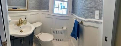 Bathroom with a white toilet, sink with gold faucet, and blue towel. Walls are white with textured blue wallpaper.