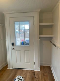 White door with glass pane, built-in shelves, and hooks, in a small room with wood-look flooring.