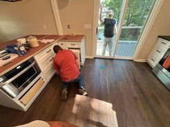 Two men installing kitchen cabinets; one is reaching, the other is leaning near a sliding glass door.