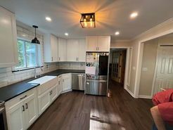 Kitchen with white cabinets, black countertops, stainless steel appliances, and dark wood floors.