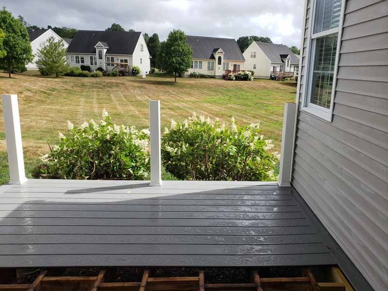 Gray deck with white posts, overlooking a grassy yard and houses under a cloudy sky.