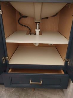Bathroom vanity cabinet interior with two shelves and a drawer. Dark blue doors and beige shelving.