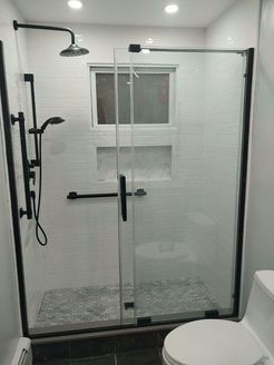 Black-framed glass shower with white tiled walls, black fixtures, and a window.