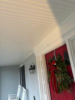 Red front door with holiday wreath, under a white porch ceiling.