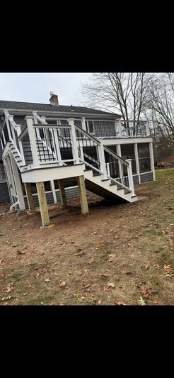 A white two-story house with a wooden deck and stairs. The yard is covered in brown leaves.