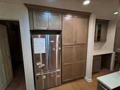 Kitchen with stainless steel refrigerator and pantry cabinets. Built-in desk area. Brown cabinets, light wood floor.