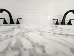 White marble countertop with black faucets against a white tiled backsplash.
