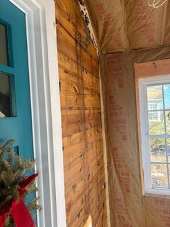 Interior view of a building under construction. Wood paneling on one wall, insulation on another, and a teal door.