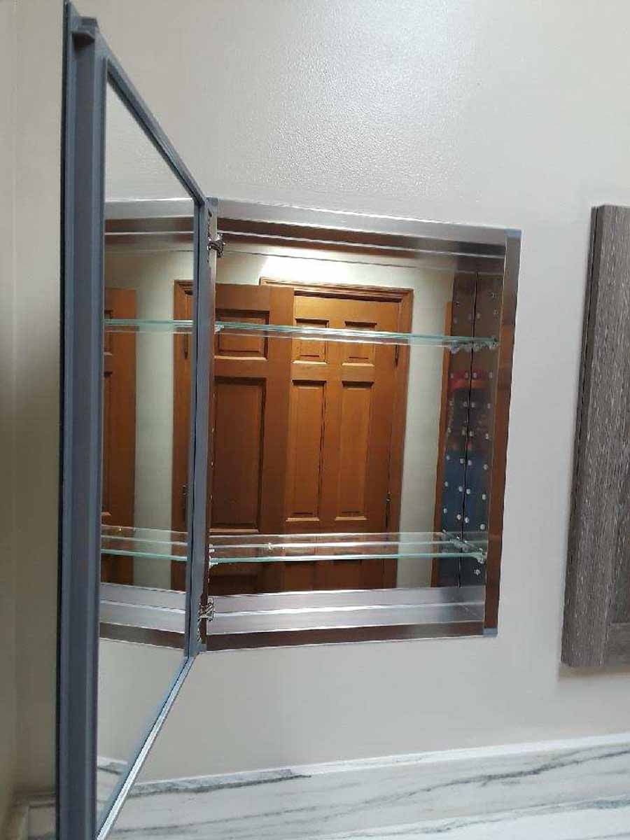 Open medicine cabinet with mirrored door, stainless steel frame. Interior shows shelves, wooden door reflection.
