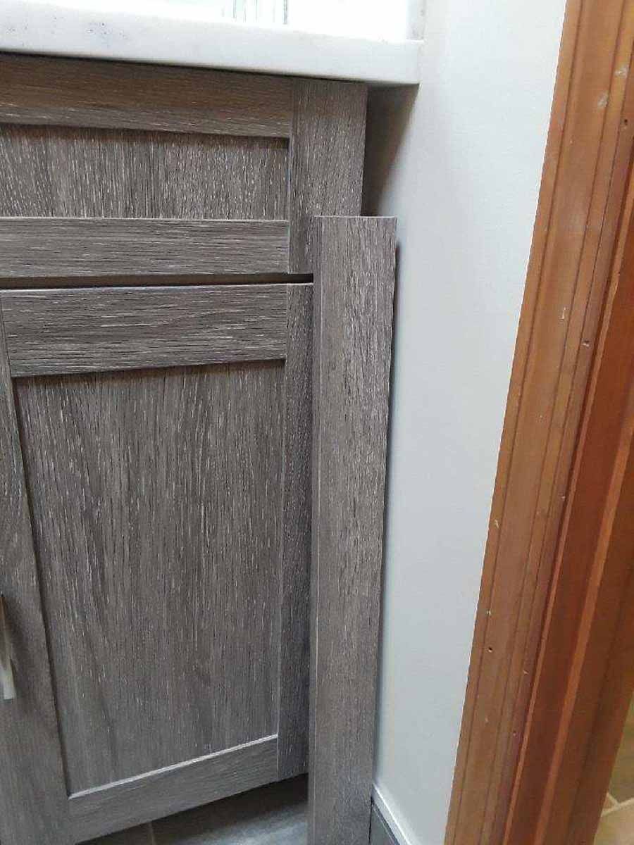 Gray wood-grain cabinet with a matching panel leaning against the wall next to a white wall and brown door.