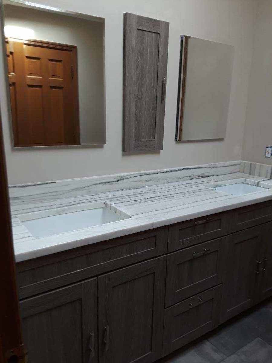 Bathroom vanity with gray cabinets, marble countertop, mirrors, and a wooden door.