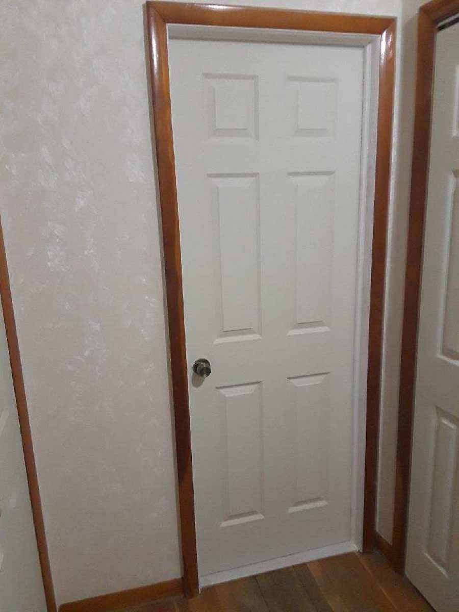 White six-panel door with brown trim in a room with light-colored walls and floor.