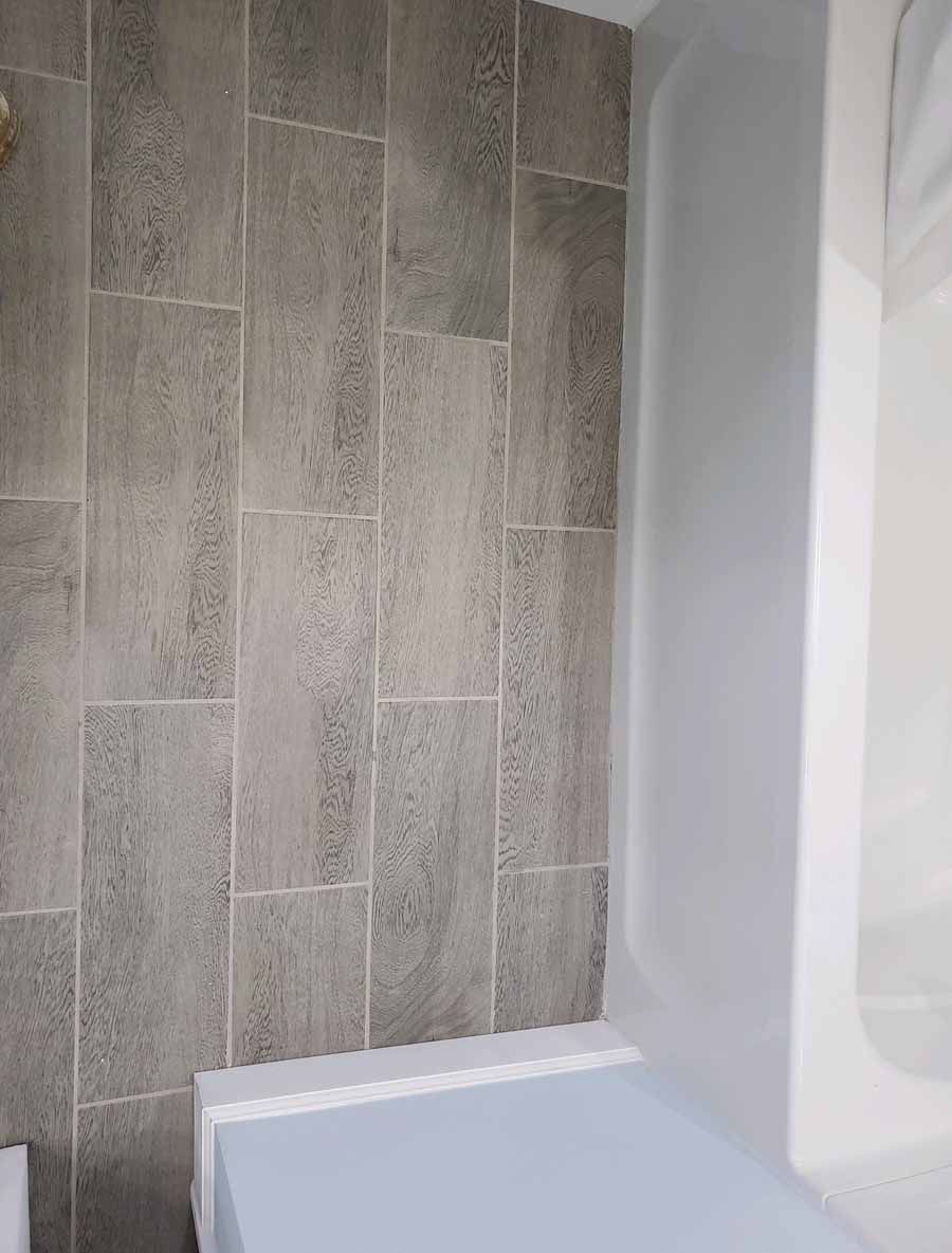 Gray tiled bathroom wall next to a white tub and shower enclosure.