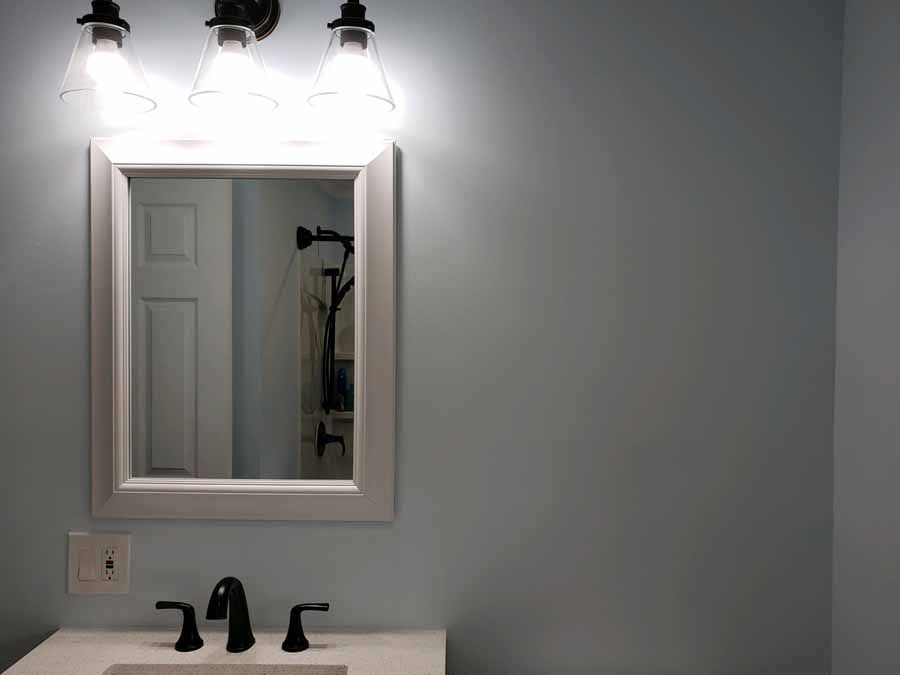 Bathroom with a white-framed mirror, sink, black faucet, and three-light fixture on a blue wall.