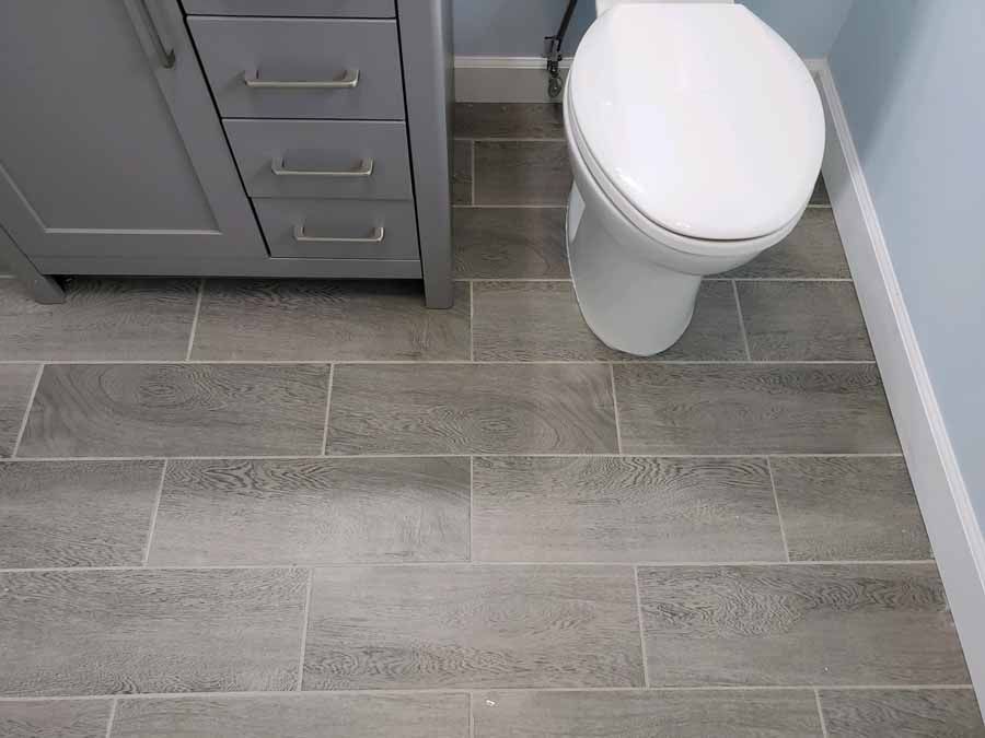 Gray tiled bathroom floor with a toilet, cabinet, and blue wall.