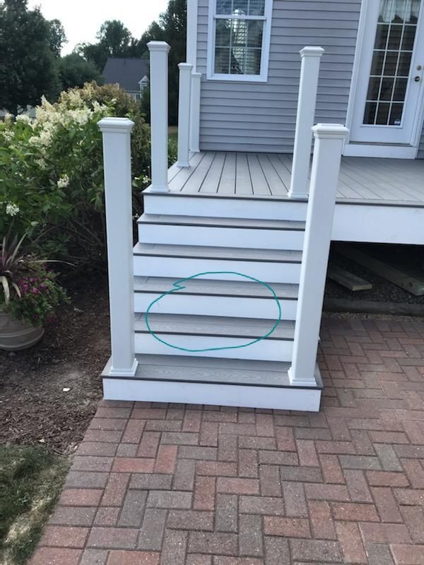 Grey composite stairs leading up to a deck with white railings. Brick patio.
