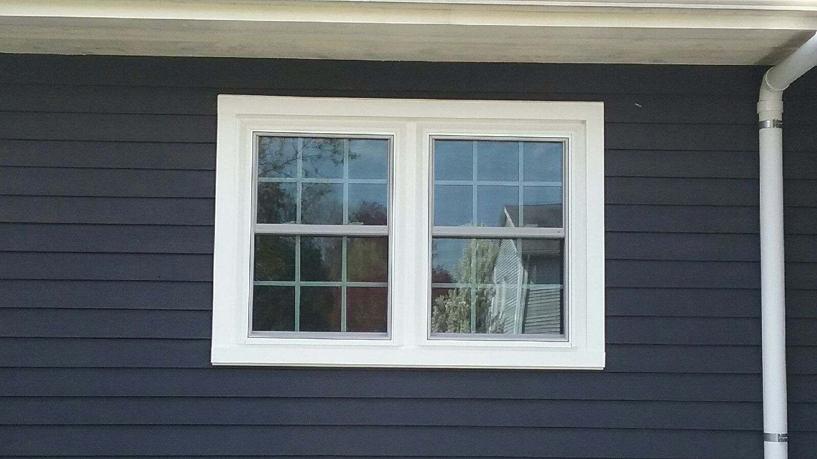 White-framed double-hung window on dark blue siding. White trim and gutter visible.