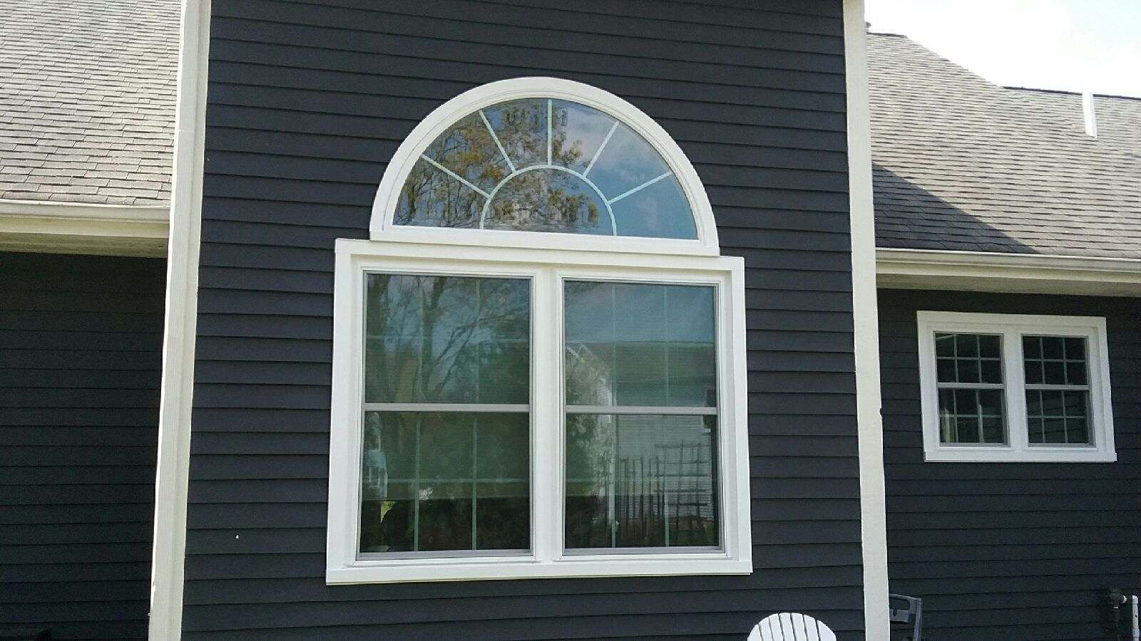 Dark siding with white trim framing a window. An arched window is above the main window on a house.