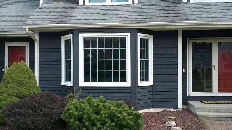 Dark blue house with white trim, bay window, and red doors.