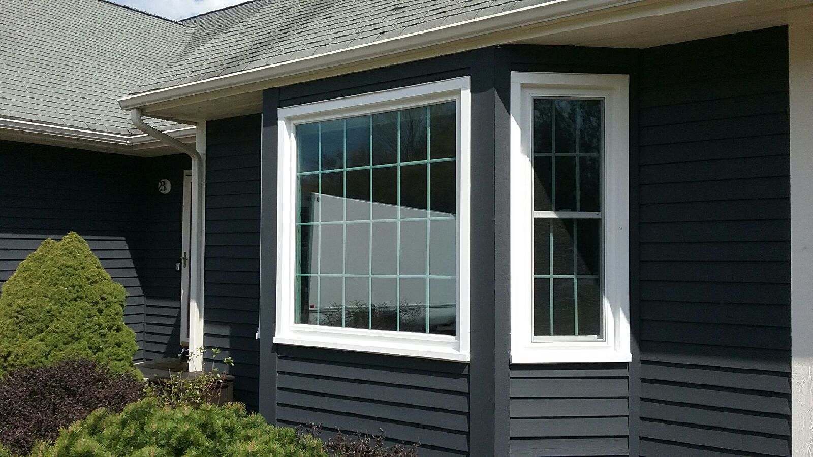Dark gray house exterior with white-framed bay window, siding, and shrubs in front.