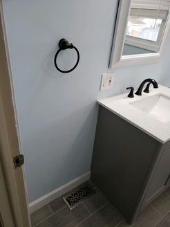 Bathroom with light blue walls, gray vanity, black faucet and towel ring, and a window.
