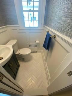 Small bathroom with white walls, herringbone tile floor, toilet, and sink. Window at the back.