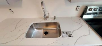 Kitchen counter with stainless steel sink, faucet, and outlet. White marble pattern on the countertop.