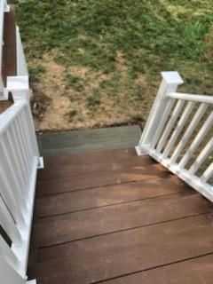 Brown wooden deck stairs with white railings leading to a grassy area.