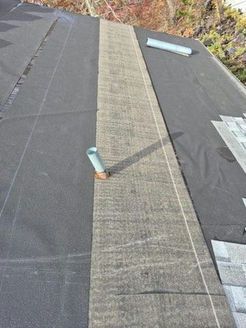 Roof with dark underlayment, gray strip, a pipe, and roofing tiles.
