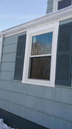 Blue siding with white-trimmed window and gray shutters; snow on the ground; blue sky.