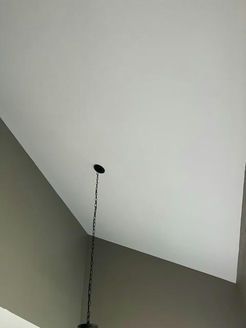 Angled white ceiling with a dark light fixture hanging from a circular opening.