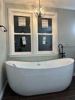 Modern white bathtub under windows in a bathroom, with a black faucet and a crystal chandelier.