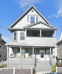 Gray multi-story house with front porches and a peaked roof.